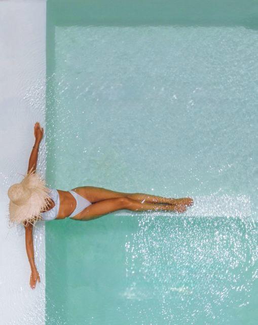 Woman wearing a straw hat relaxing on the edge of a turquoise swimming pool at a luxury hotel
