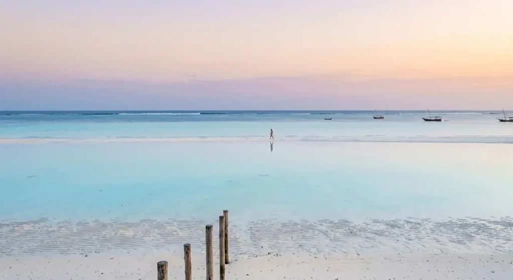 A person walking on a mirror-like sandbank in Paje at low tide, reflecting a slow living vibe.