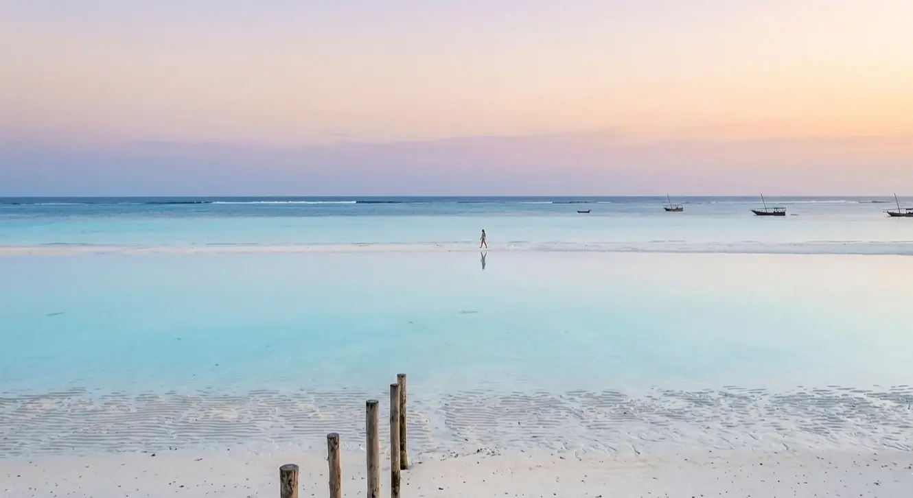 A person walking on a mirror-like sandbank in Paje at low tide, reflecting a slow living vibe.