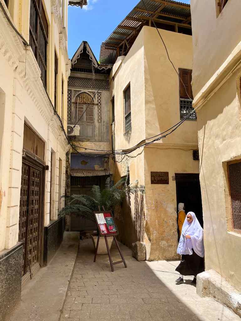 Woman in traditional attire walking past historic buildings in Stone Town, Zanzibar