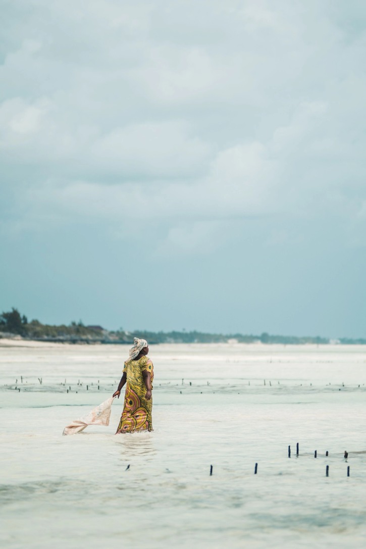 Woman in traditional dress walking through shallow ocean waters at Jambiani in Zanzibar