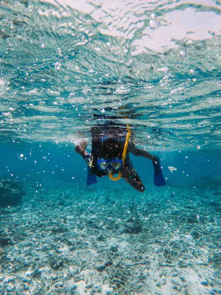 Person swimming underwater with a yellow snorkel and blue mask in clear sea wate