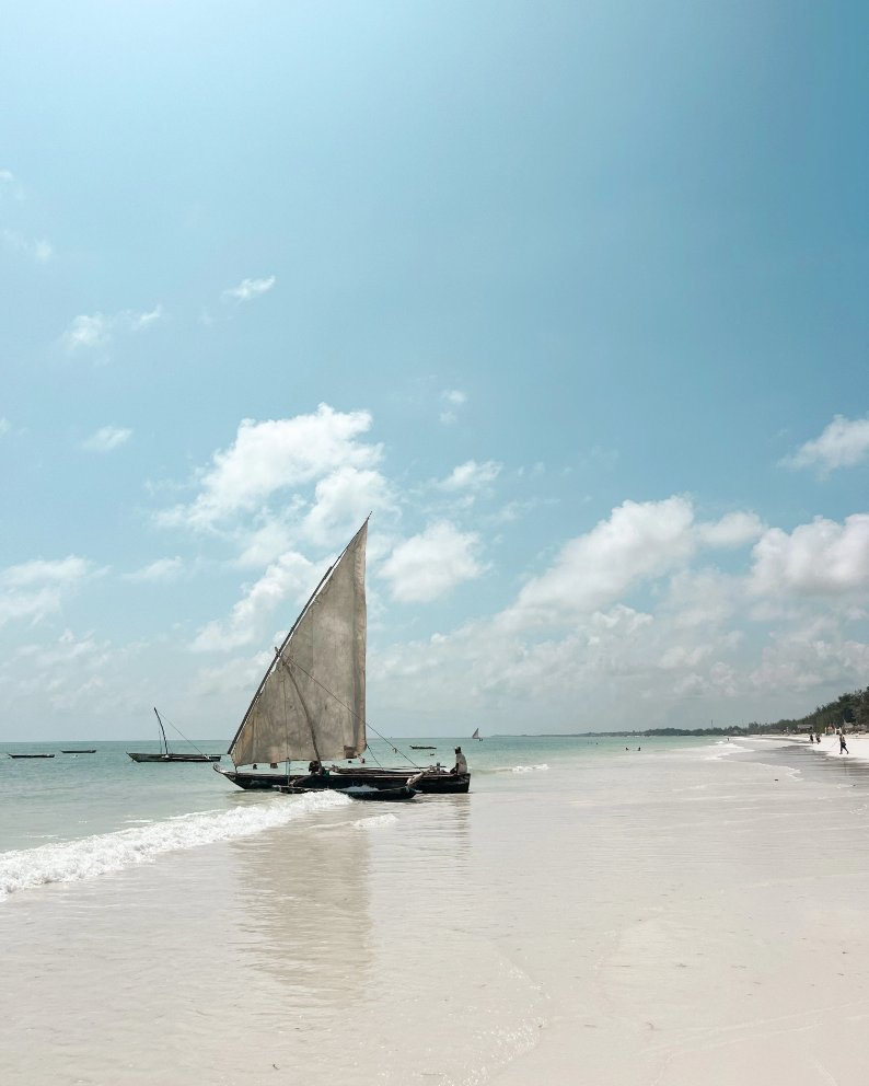 Traditional dhow boat floating in shallow ocean water along Mtende Beach in Zanzibar