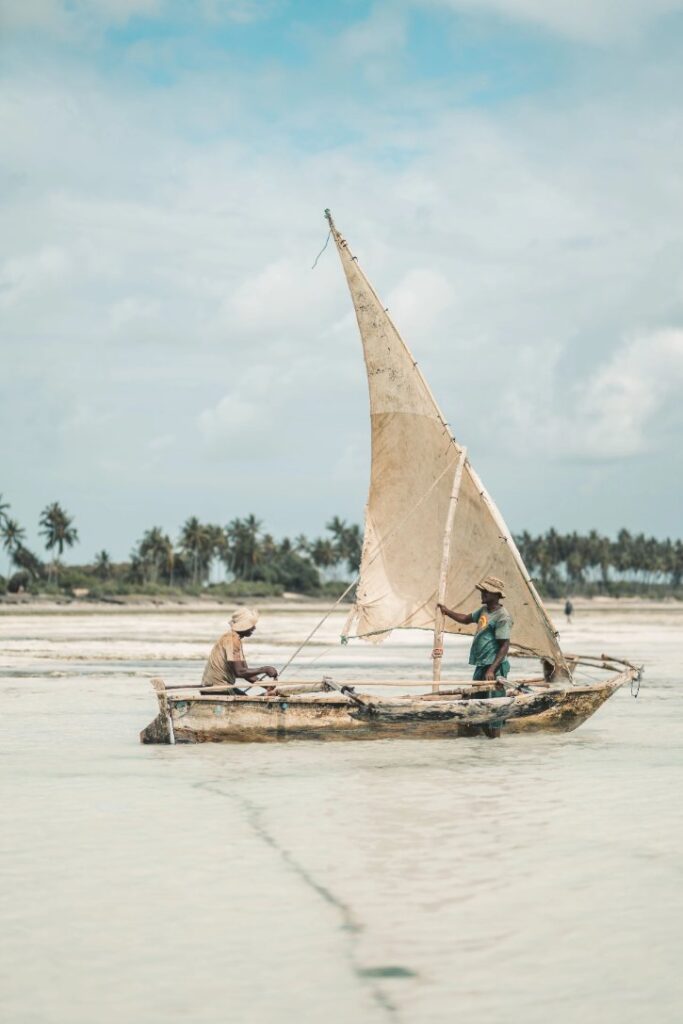 Two fishermen navigating a traditional wooden dhow boat on the water in Makunduchi