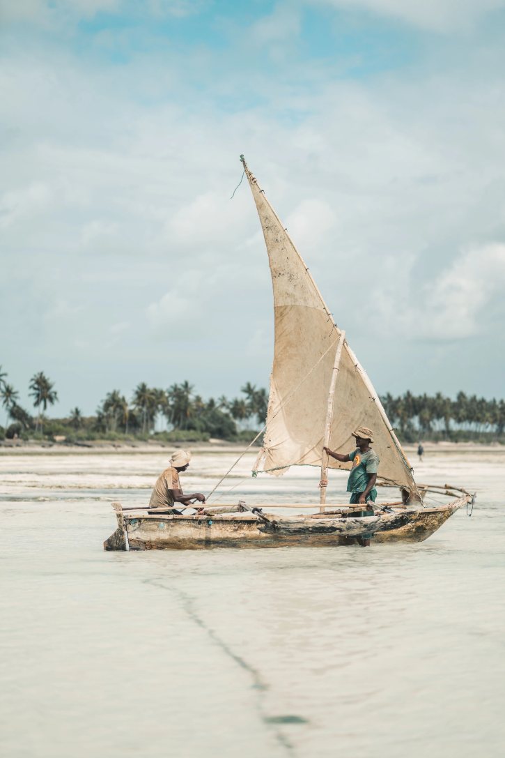 Two fishermen navigating a traditional wooden dhow boat on the water in Makunduchi